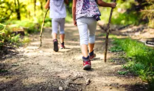 Zwei Kinder wandern mit Wanderschuhen und Stöcken auf einem Wanderweg.