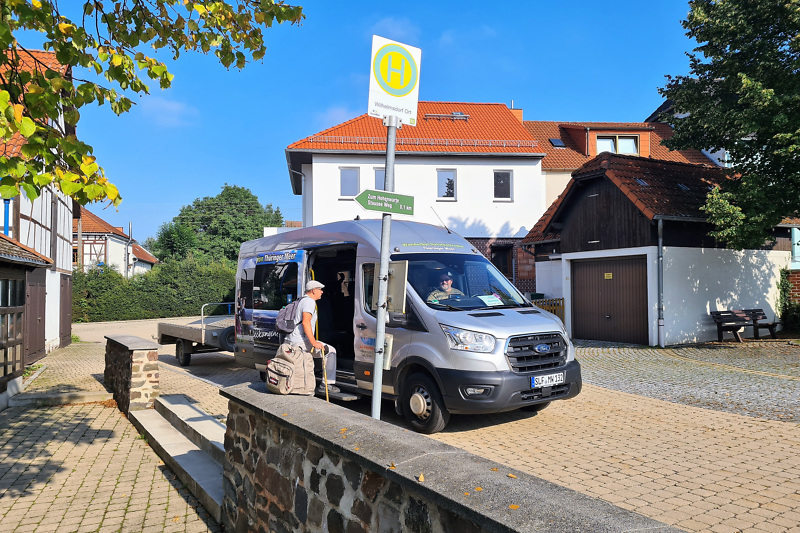 Ein Wanderbus der KomBus hält an einer Haltestellen. Eine Person steigt ein.