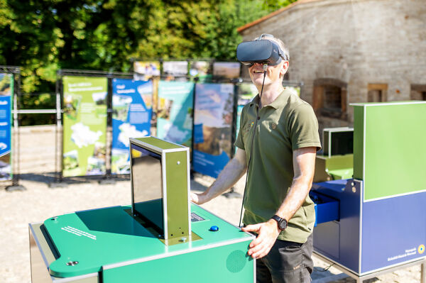 Ein Mann steht an einem interaktiven Cube der Wanderausstellung "Lass dich begeistern!" und schaut begeistert in eine Virtual Reality-Brille.