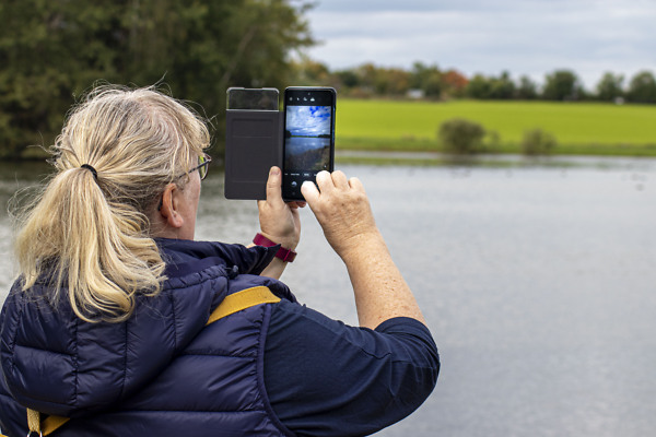 Eine Frau fotografiert mit ihrem Handy eine Teichlandschaft im Naturpark.